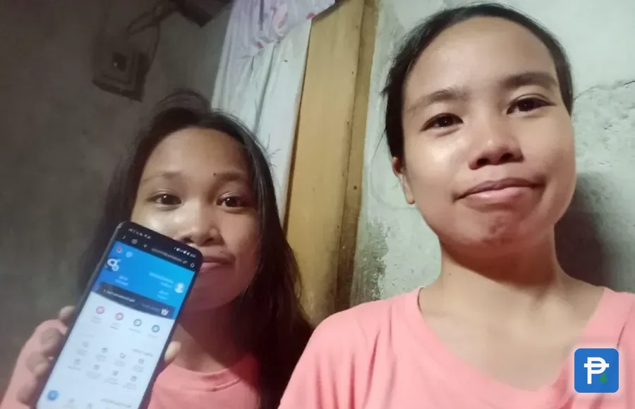 Two women indoors taking a selfie, one of them holding a phone on the Novaluxia account screen