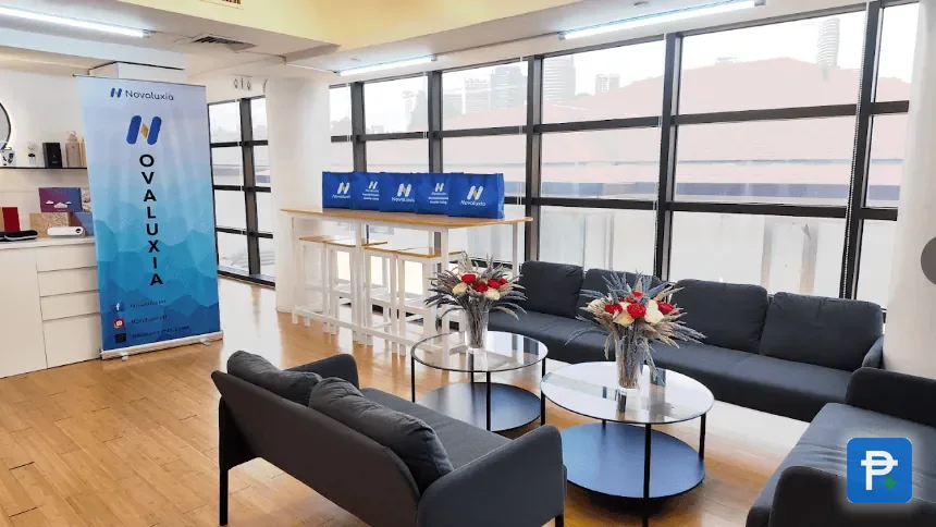 Novaluxia office lounge with grey sofas, round coffee tables and a roller banner by a window